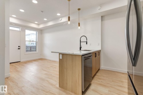 Contemporary kitchen island featuring a light-toned wood-finish base, integrated stainless steel dishwasher, and a white countertop with an undermount sink - #1 16231 19 Av Sw, Edmonton, AB - Indoor Photo Showing Kitchen With Upgraded Kitchen