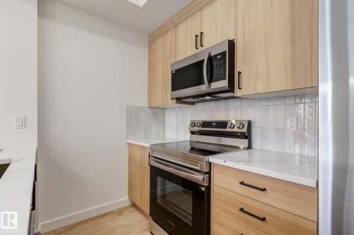 Contemporary kitchen featuring light wood-finish cabinetry with matte black hardware, stainless steel appliances, white subway tile backsplash, and light-toned countertops - #1 16231 19 Av Sw, Edmonton, AB - Indoor Photo Showing Kitchen