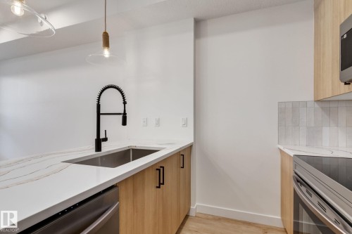 Kitchen featuring light wood-finish cabinetry, white countertops with veining, a stainless steel undermount sink with a black coiled faucet, and a light tile backsplash - #1 16231 19 Av Sw, Edmonton, AB - Indoor Photo Showing Kitchen