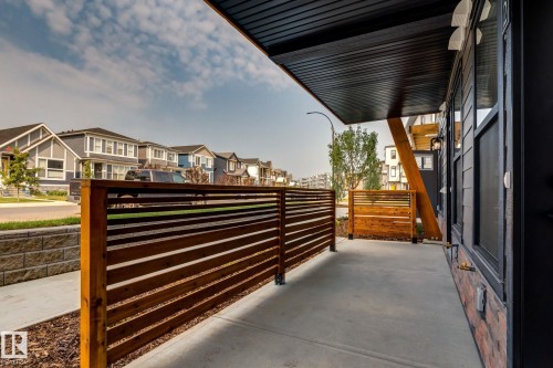 Spacious concrete patio featuring horizontal wood-slat privacy screens, a black corrugated ceiling overhang, and a brick veneer exterior accent - #1 16231 19 Av Sw, Edmonton, AB - Outdoor With Exterior