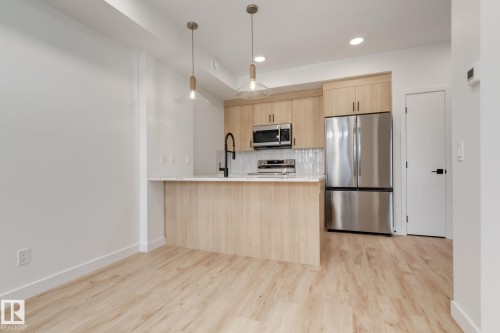 Open-concept kitchen featuring light wood-finish cabinetry and a white countertop island with seating - #1 16231 19 Av Sw, Edmonton, AB - Indoor Photo Showing Kitchen