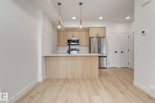 Kitchen featuring light wood-finish cabinetry, stainless steel appliances, a white tile backsplash, and a breakfast bar with a light-toned countertop - #1 16231 19 Av Sw, Edmonton, AB - Indoor Photo Showing Kitchen