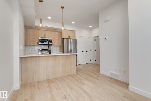 Kitchen area featuring light wood-finish cabinetry, stainless steel appliances, and a breakfast bar with pendant lighting - #1 16231 19 Av Sw, Edmonton, AB - Indoor Photo Showing Kitchen