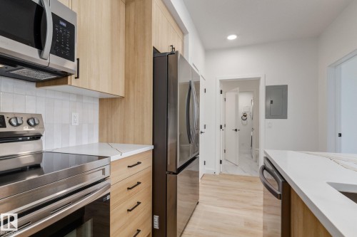 Kitchen featuring light wood-finish cabinetry, stainless steel appliances, white tile backsplash, and light countertops - #1 16231 19 Av Sw, Edmonton, AB - Indoor Photo Showing Kitchen