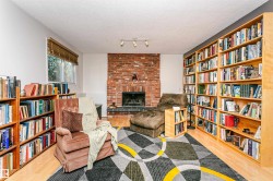 Room featuring a brick fireplace with a dark stone hearth, wood-finish flooring, two walls of built-in shelving, and a window with a woven wood blind - 