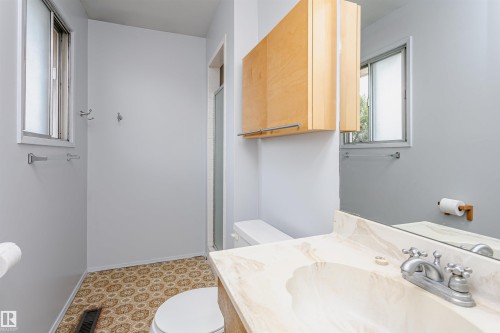 Bathroom featuring a vanity with an integrated sink and light-toned countertop, a wood-finish overhead cabinet, and a window with frosted glass - 18316 78 Avenue Nw, Edmonton, AB - Indoor Photo Showing Bathroom