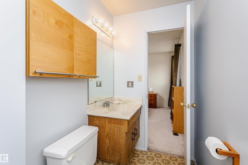 Bathroom featuring a light wood-finish vanity with a light-toned countertop, a wall-mounted mirror, and a coordinating wood-finish wall cabinet - 18316 78 Avenue Nw, Edmonton, AB - Indoor Photo Showing Bathroom