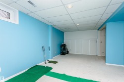 Spacious room featuring light blue painted walls, light-colored carpeting, a drop ceiling, recessed lighting, and a small egress window - 
