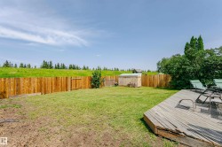 Expansive backyard featuring a wood deck, a wood privacy fence, a storage shed, and a verdant treeline beyond the property boundary - 