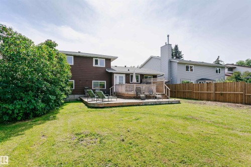 Expansive backyard featuring a large wooden deck with lattice railing, a manicured lawn, a mature tree, and a brown siding exterior - 18316 78 Avenue Nw, Edmonton, AB - Outdoor With Deck Patio Veranda