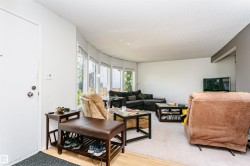 Living area featuring a curved wall of windows, textured ceiling, light wood-finish flooring, and a white entry door with brass hardware - 