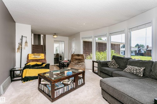 Living room featuring curved wall of windows, textured ceiling, light-toned carpet, and a wooden staircase - 18316 78 Avenue Nw, Edmonton, AB - Indoor Photo Showing Living Room