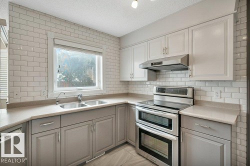 Kitchen featuring two-tone cabinetry with light grey base cabinets and white upper cabinets, subway tile backsplash, and stainless steel appliances including a double oven range and high air flow hood fan. - 568 Buchanan Road Nw, Edmonton, AB - Indoor Photo Showing Kitchen With Double Sink