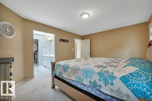 Carpeted room with a ceiling-mounted light fixture, warm-toned walls, and a doorway opening to a bathroom featuring a double vanity with white cabinetry and a walk-in closet - 568 Buchanan Road Nw, Edmonton, AB - Indoor Photo Showing Bedroom