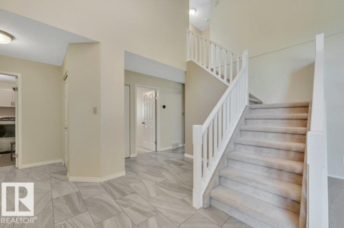 Foyer featuring light-toned tile flooring, a carpeted staircase with white railings. - 568 Buchanan Road Nw, Edmonton, AB - Indoor Photo Showing Other Room