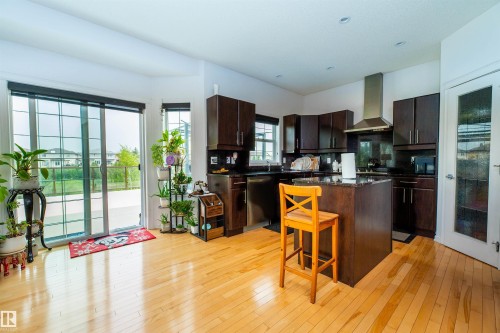 Open-concept kitchen with wood-finish flooring, dark wood cabinetry, a central island with a stone countertop, stainless steel appliances, and a glass sliding door leading to an outdoor area - 715 Wildwood Point(E) Nw, Edmonton, AB - Indoor Photo Showing Kitchen
