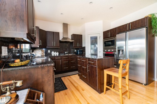 Kitchen featuring dark wood-finish cabinetry, granite countertops, stainless steel appliances, a central island, and light wood-finish flooring - 715 Wildwood Point(E) Nw, Edmonton, AB - Indoor Photo Showing Kitchen