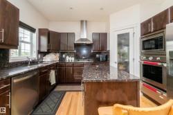 Kitchen featuring wood cabinetry, stone countertops, stainless steel appliances, a center island, and wood-finish flooring - 