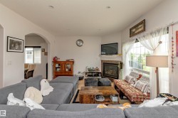 Spacious living area featuring a corner fireplace with a stone surround and mantel, wood-finish flooring, and an arched doorway opening to an additional room - 
