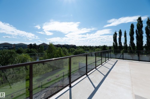 Spacious outdoor patio area featuring a glass railing system, concrete flooring, and surrounding mature trees - 715 Wildwood Point(E) Nw, Edmonton, AB - Outdoor With View