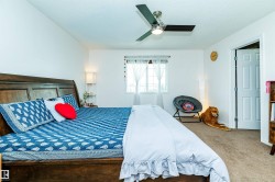 Spacious bedroom featuring a wood-finish bed frame, light-colored carpeting, a multi-pane window, and a ceiling fan with integrated lighting - 
