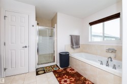 Bathroom featuring a built-in soaking tub with chrome fixtures, a separate glass-enclosed shower, white paneled door, and neutral tile flooring - 