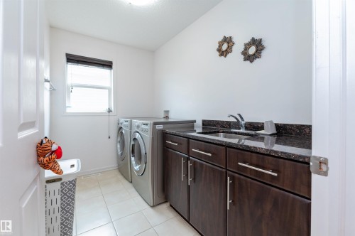 Laundry room featuring a utility sink with a stone countertop, dark wood-finish cabinetry with silver hardware, and tile flooring - 715 Wildwood Point(E) Nw, Edmonton, AB - Indoor Photo Showing Laundry Room