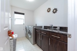 Laundry room featuring a utility sink with a stone countertop, dark wood-finish cabinetry with silver hardware, and tile flooring - 