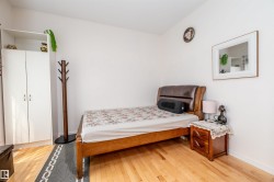 Hardwood-style flooring throughout the room, complemented by a built-in white wardrobe with double doors and an upper open shelf - 