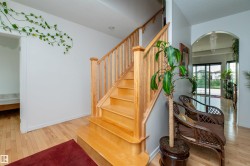 Natural wood staircase with matching railing and balusters, wood-finish flooring, recessed lighting, and an arched doorway leading to an interior space with sliding glass doors - 