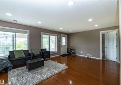 Spacious living area featuring rich wood-finish flooring, recessed lighting, expansive windows, and a white paneled door leading to an additional space - 