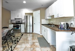 Kitchen featuring light-toned tile flooring, white cabinetry, dark speckled countertops, stainless steel appliances, and a tiled backsplash - 