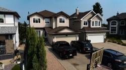 Two-story residence featuring light-colored siding, a multi-pitched brown shingle roof, and white-framed windows - 
