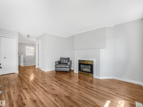 Living area featuring wood-finish flooring, a white mantel, and an integrated fireplace with a black and brass surround - #2 3311 58 St Nw, Edmonton, AB - Indoor Photo Showing Living Room With Fireplace