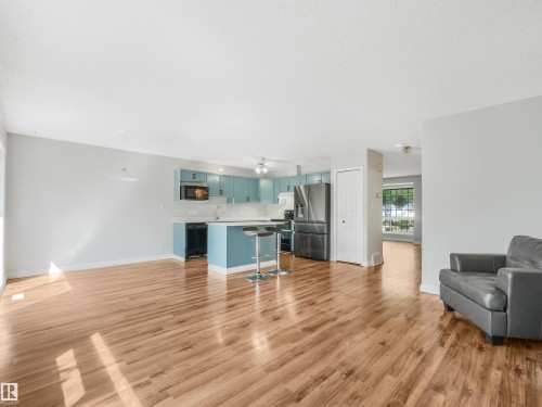 Open-concept living space featuring wood-finish flooring, a kitchen island with seating, light blue cabinetry, and stainless steel appliances - #2 3311 58 St Nw, Edmonton, AB - Indoor Photo Showing Living Room