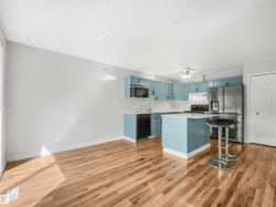 Open-concept kitchen and dining area featuring wood-finish flooring, a kitchen island with seating, light blue cabinetry, and stainless steel appliances - 