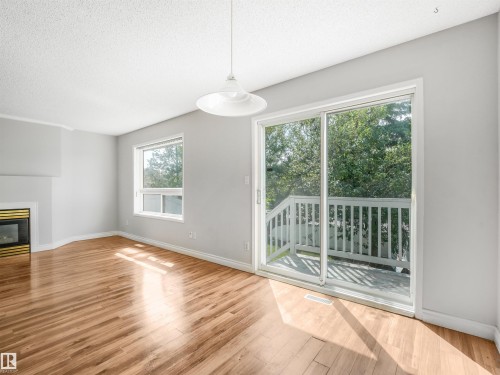 Sliding glass door opening to an outdoor deck with white railing - #2 3311 58 St Nw, Edmonton, AB - Indoor With Fireplace