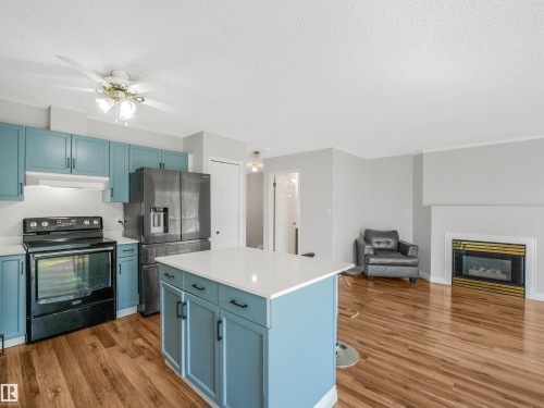 Kitchen featuring a central island with white countertop, blue cabinetry, and stainless steel appliances - #2 3311 58 St Nw, Edmonton, AB - Indoor Photo Showing Kitchen With Fireplace