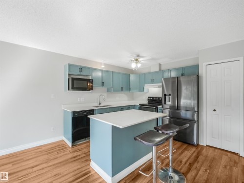 Contemporary kitchen featuring light blue cabinetry, white countertops, stainless steel appliances, and wood-finish flooring - #2 3311 58 St Nw, Edmonton, AB - Indoor Photo Showing Kitchen With Upgraded Kitchen
