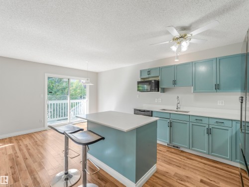 Kitchen with teal cabinetry, white countertops, and wood-finish flooring - #2 3311 58 St Nw, Edmonton, AB - Indoor Photo Showing Kitchen With Upgraded Kitchen