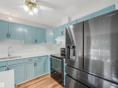 Kitchen featuring perimeter cabinetry with a light blue finish, white countertops, stainless steel appliances, and wood-finish flooring - #2 3311 58 St Nw, Edmonton, AB - Indoor Photo Showing Kitchen