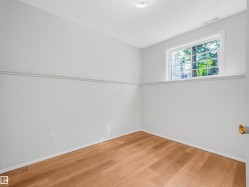 Room featuring light wood-finish flooring, light gray walls with a chair rail, a white-framed window with security bars, and a flush-mount ceiling light fixture - 
