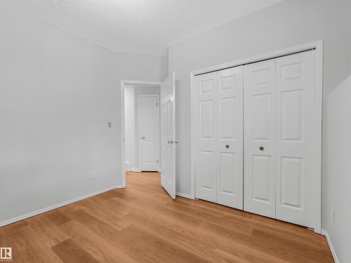 Room featuring wood-finish flooring, light gray walls, a white bi-fold closet, and a white interior door - #2 3311 58 St Nw, Edmonton, AB - Indoor Photo Showing Other Room