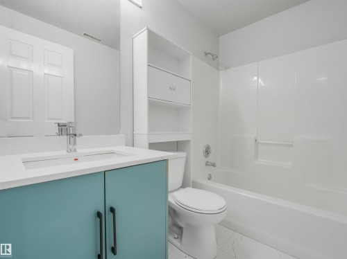 Bathroom featuring a blue vanity with a white countertop and integrated sink, chrome faucet, white toilet, and white bathtub with an integrated shower head - #2 3311 58 St Nw, Edmonton, AB - Indoor Photo Showing Bathroom