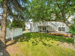 Expansive rear lawn featuring mature trees, a wooden deck, and a white privacy fence - 