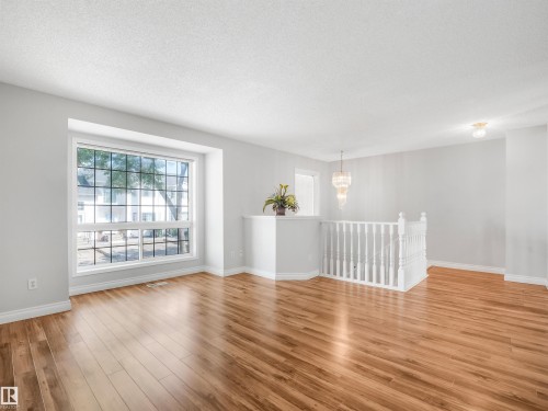 Bright living space featuring expansive bay window, wood-finish flooring, crisp white walls, and a contemporary crystal chandelier - #2 3311 58 St Nw, Edmonton, AB - Indoor Photo Showing Living Room
