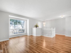 Bright living space featuring expansive bay window, wood-finish flooring, crisp white walls, and a contemporary crystal chandelier - 