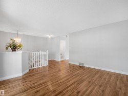 Open living space featuring wood-finish flooring, light grey wall paint, white baseboards, and a white staircase railing - 