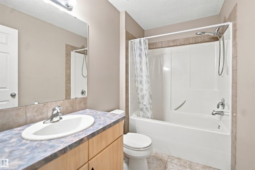 Bathroom featuring a bathtub with an integrated shower, chrome fixtures, a vanity with an undermount sink, a large wall mirror, and tile flooring - 1328 80 Street Sw, Edmonton, AB - Indoor Photo Showing Bathroom