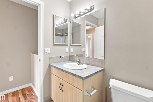 Bathroom vanity featuring a light wood-finish cabinet with black hardware, a laminate countertop, and an integrated white basin - 1328 80 Street Sw, Edmonton, AB - Indoor Photo Showing Bathroom